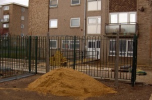 Photograph of a block of flats with newly erected railings and a pile of sand